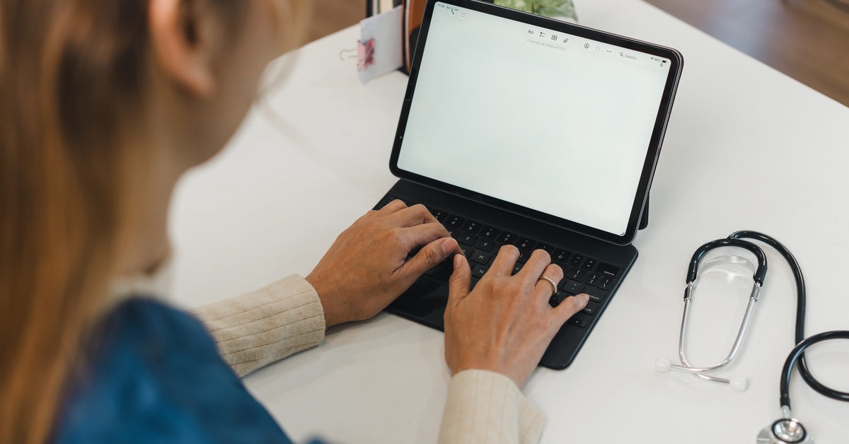 Person typing on tablet with keyboard at desk, with stethoscope nearby suggesting healthcare or medical work setting.
